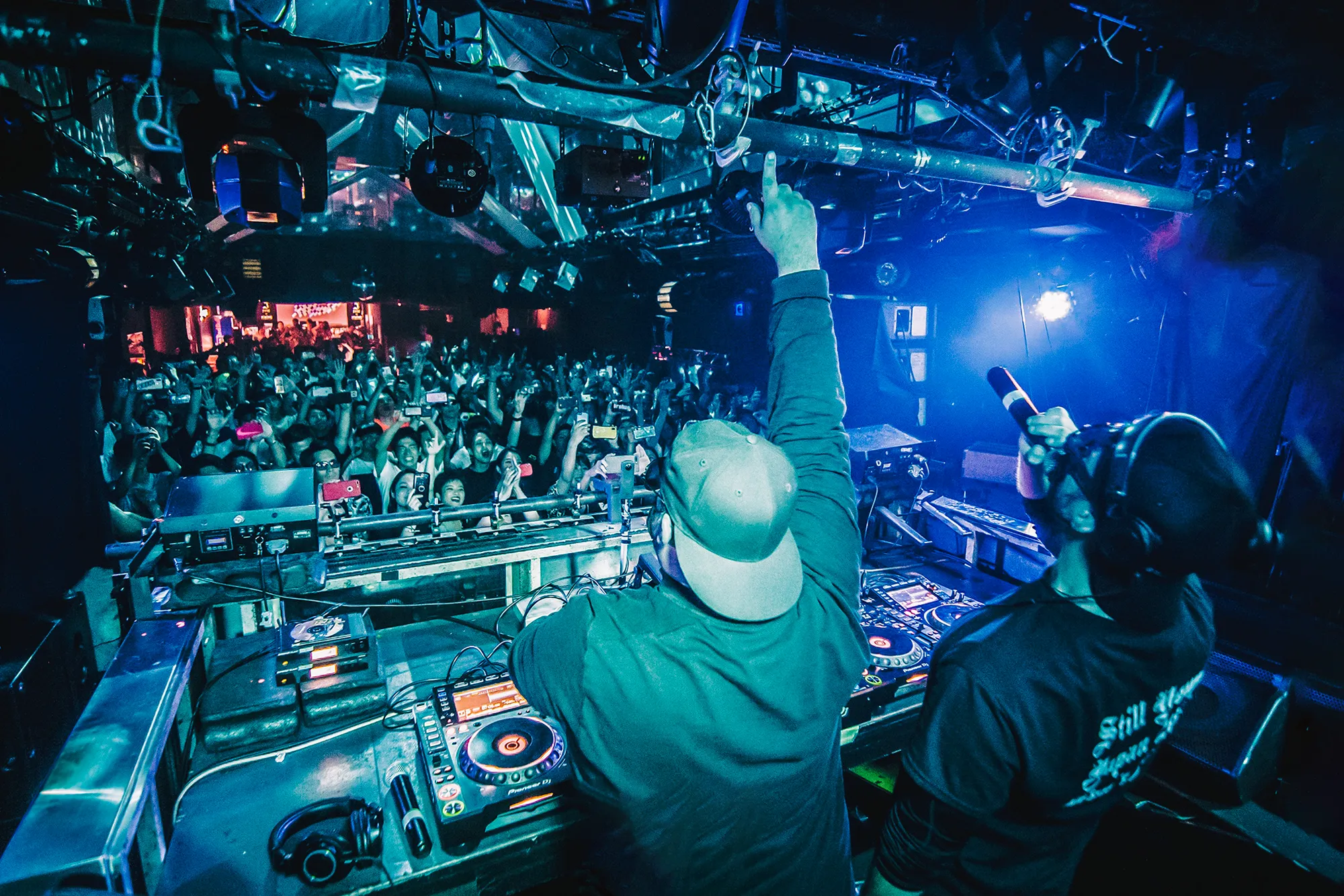 Still Young facing a packed crowd in Japan, one hand raised above the decks